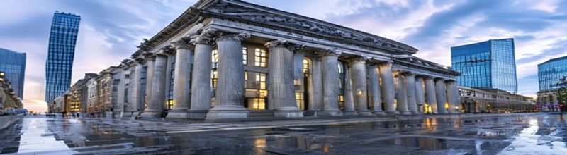 Panoramic view of the Bank of England's neoclassical Threadneedle Street facade in central London at grey morning light, tall stone columns and arched windows, surrounding modern glass City of London skyscrapers in the background, wet pavement reflecting the sky, no people no faces no hands